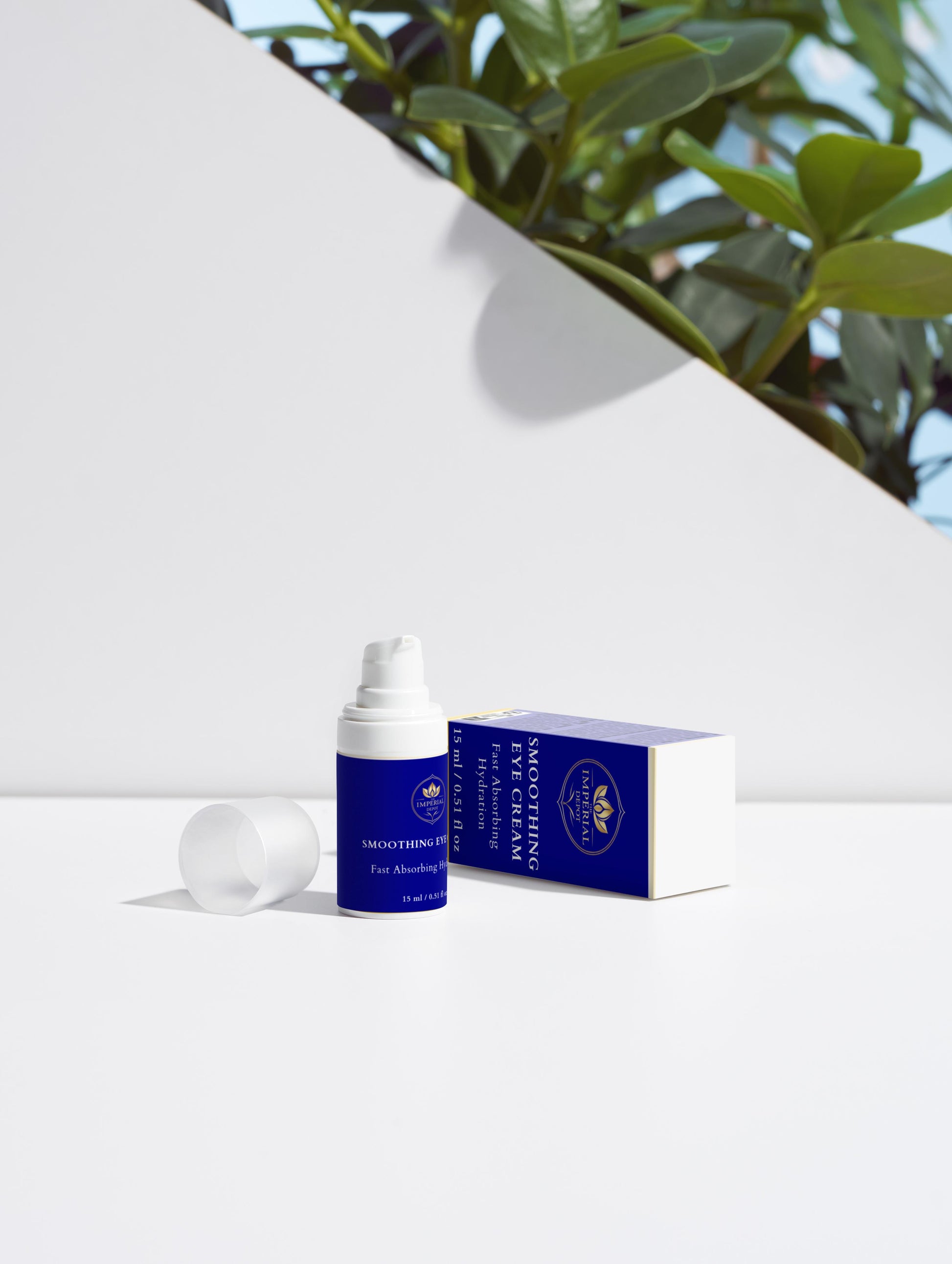Blue skincare product with white cap on a white surface with greenery in the background